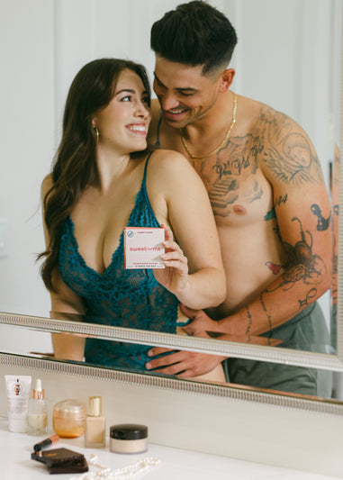 man holding woman from behind while she holds a box of sweetums wipes cherry flavor