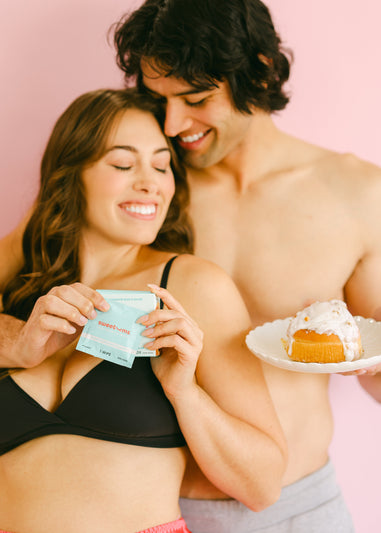 a woman and man smiling together while she holds cinnamon bun flavored intimate wipes