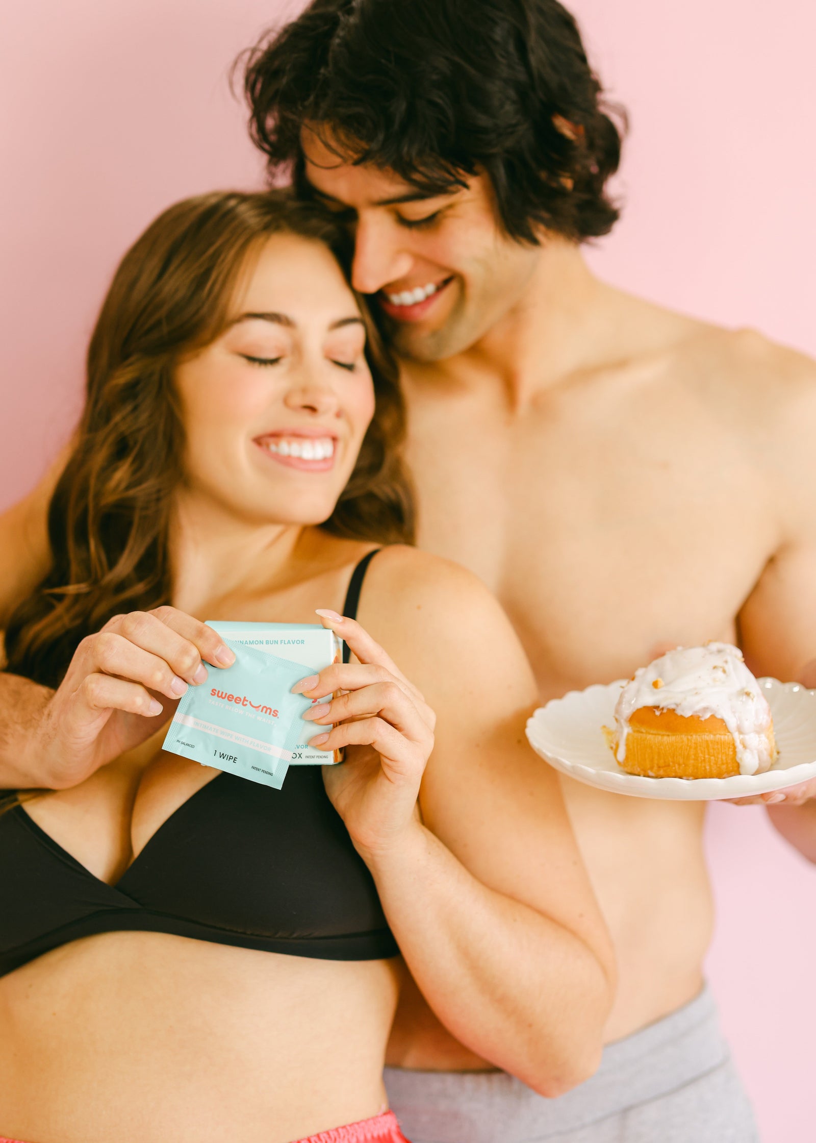 a woman and man smiling together while she holds cinnamon bun flavored intimate wipes