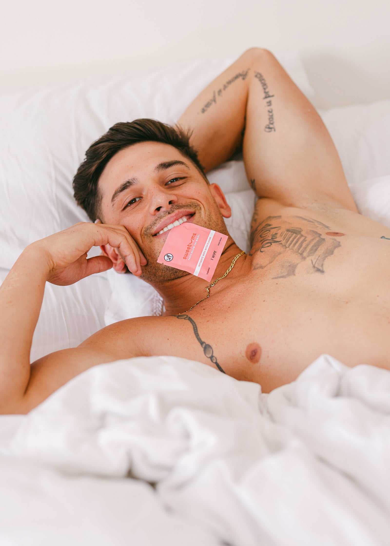 man laying in bed with a sweetums wipe in his mouth