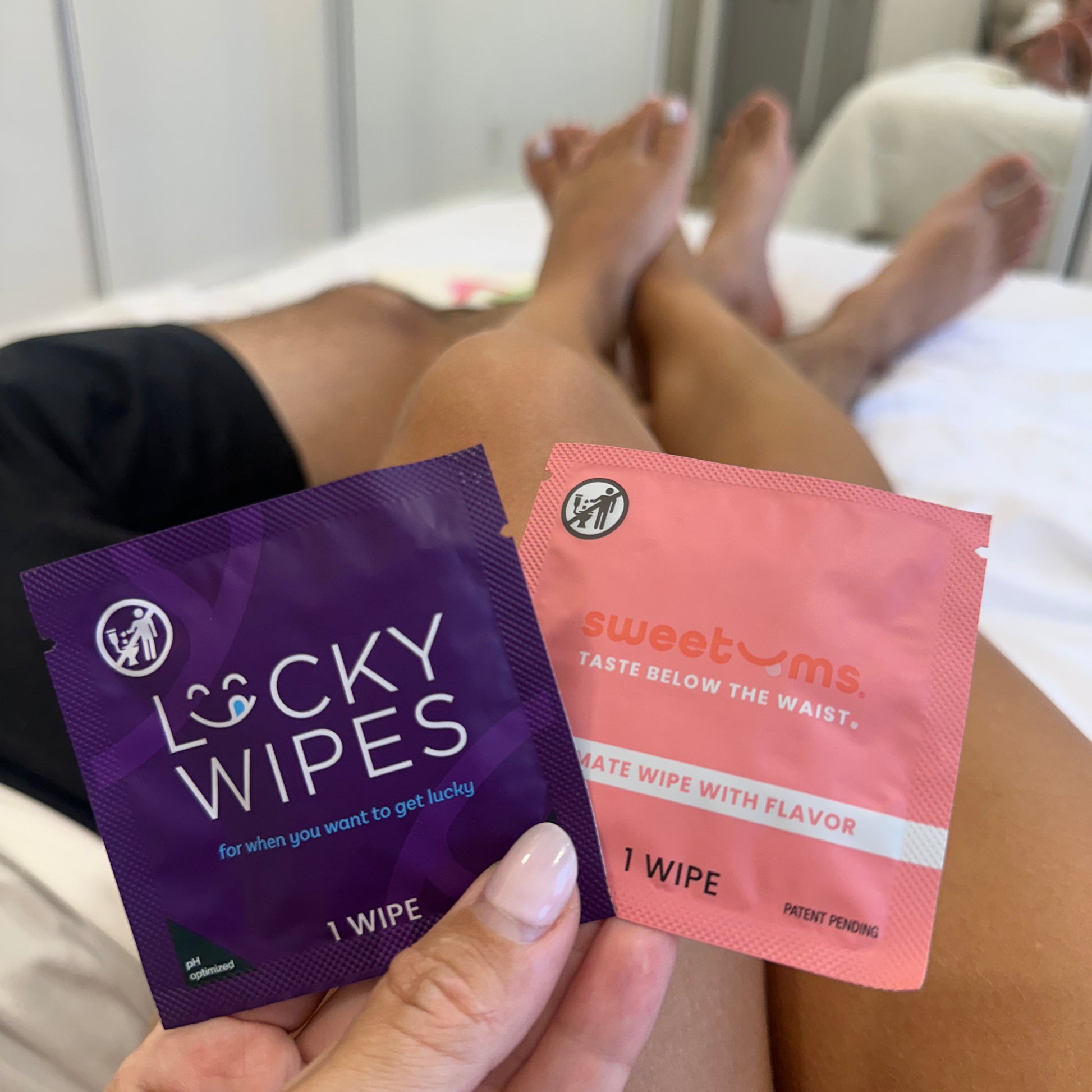 a man and woman in bed with clothes on and holding sweetums wipes and lucky wipes