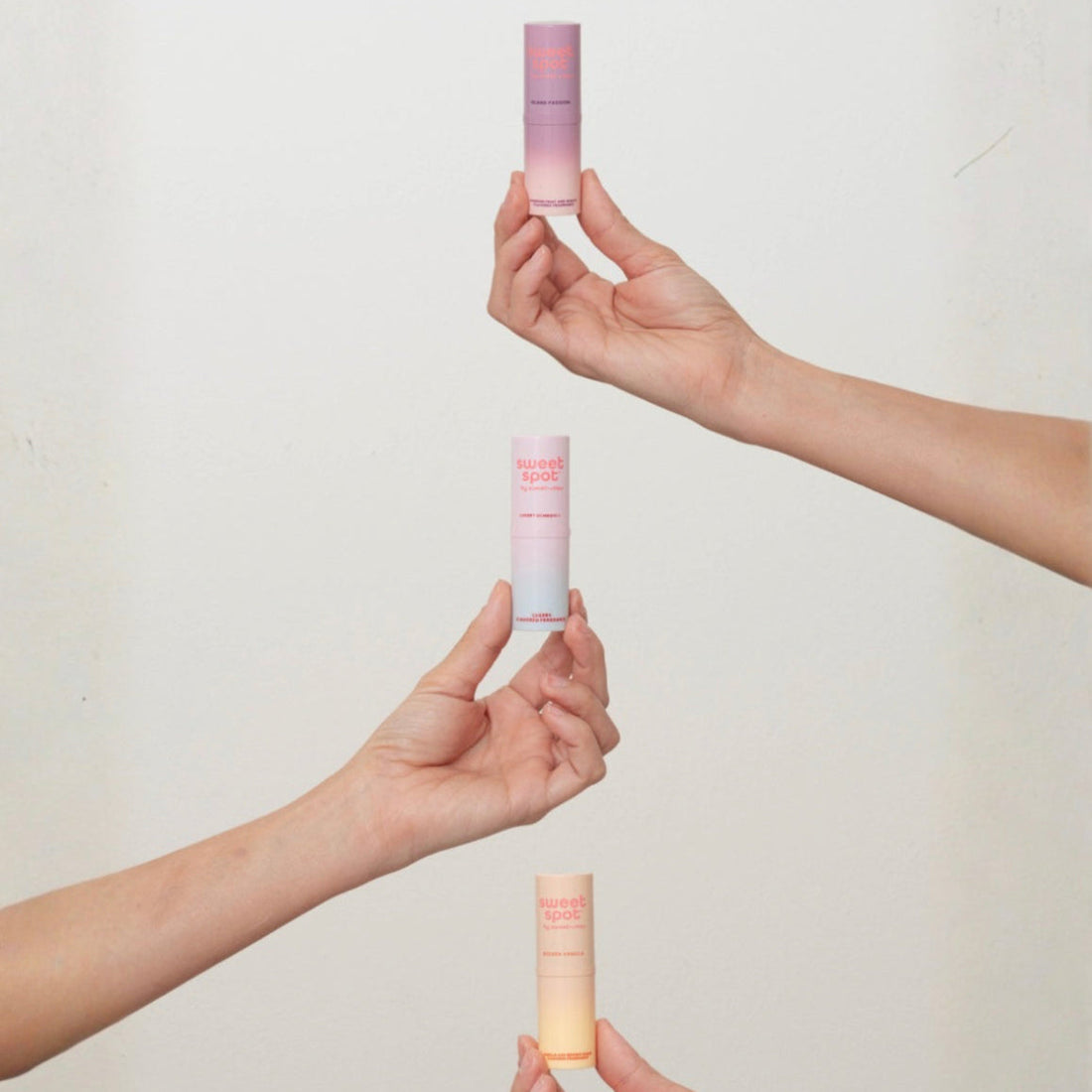 Two hands holding gradient sweet spot solid stick fragrances against a plain background