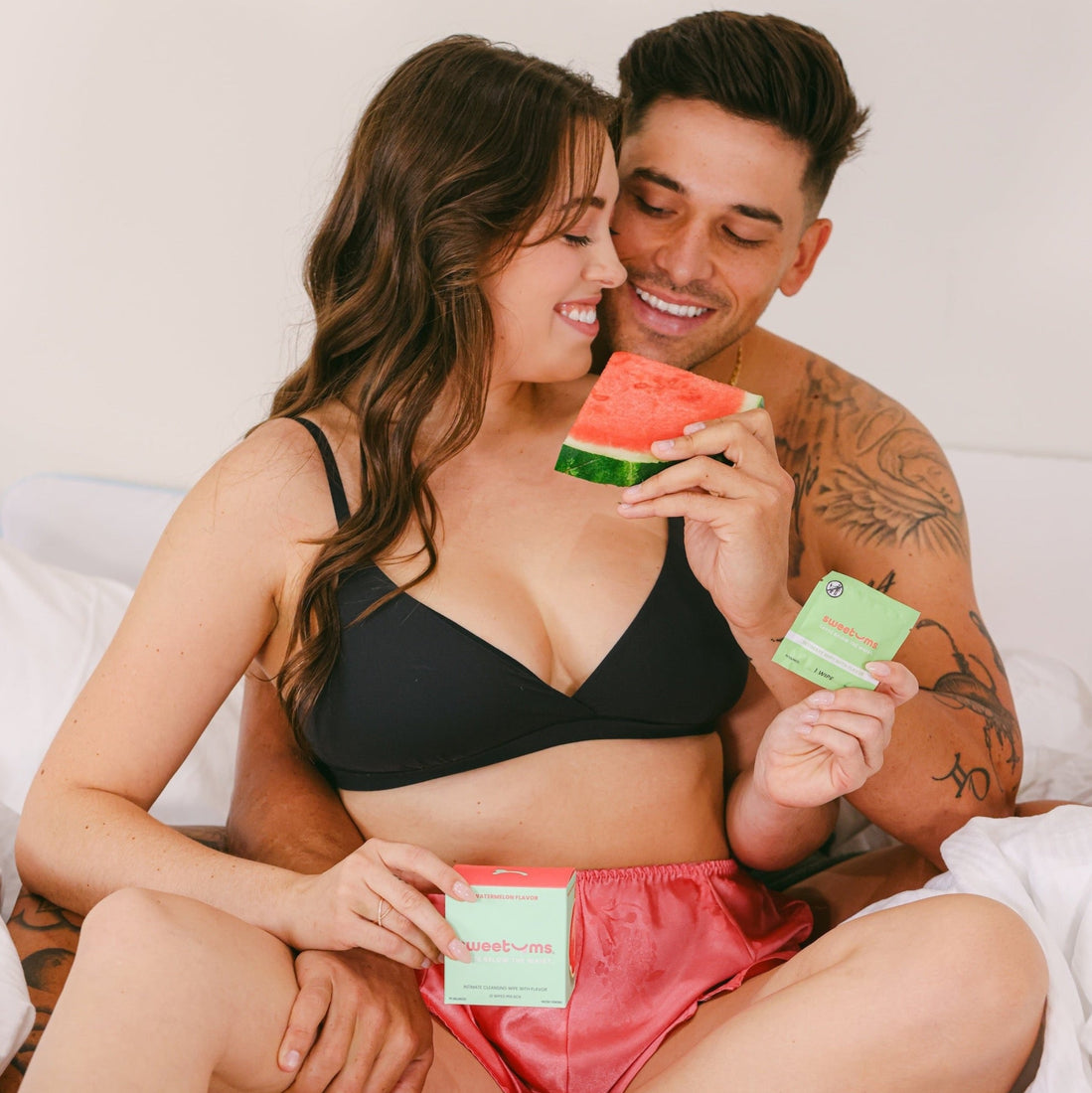 a man feeding a woman watermelon while she holds watermelon flavored intimate wipes