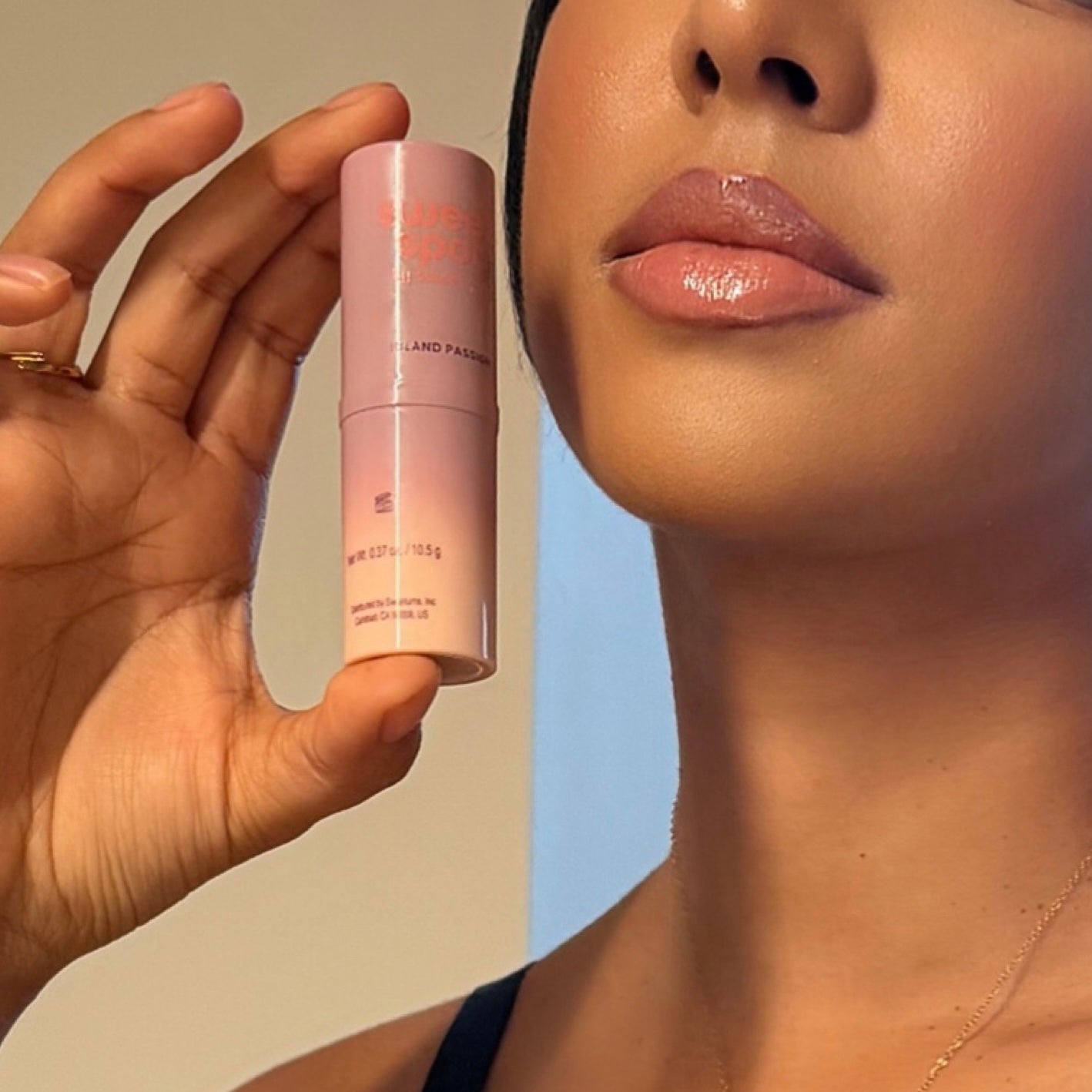 Woman holding a pink Island Passion Sweet Spot fragrance close to their face against a neutral background